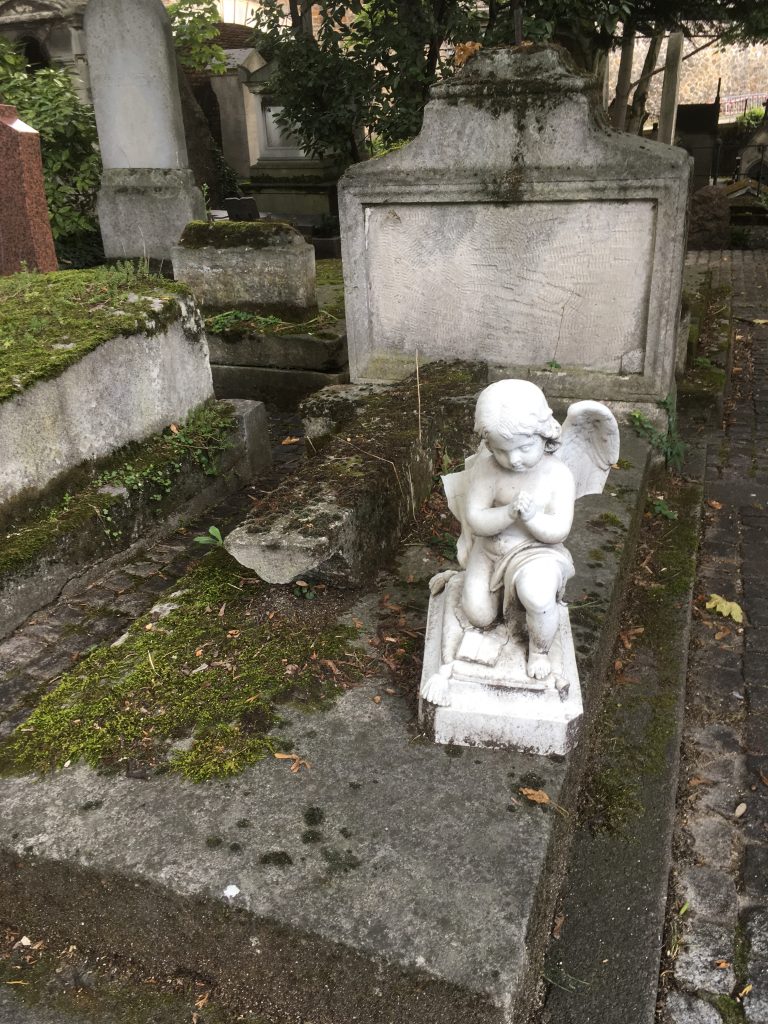 An angel with broken wings prays atop a moldering grave. Time has worn away the tomb’s engravings, and the occupant is unknown.